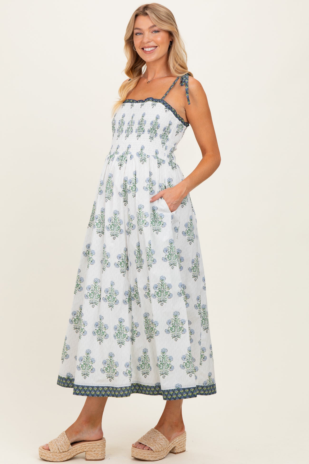 woman wearing a white floral maternity maxi dress with tied straps and pockets, showing her baby bump