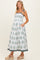 woman wearing a white floral maternity maxi dress with tied straps and pockets, showing her baby bump