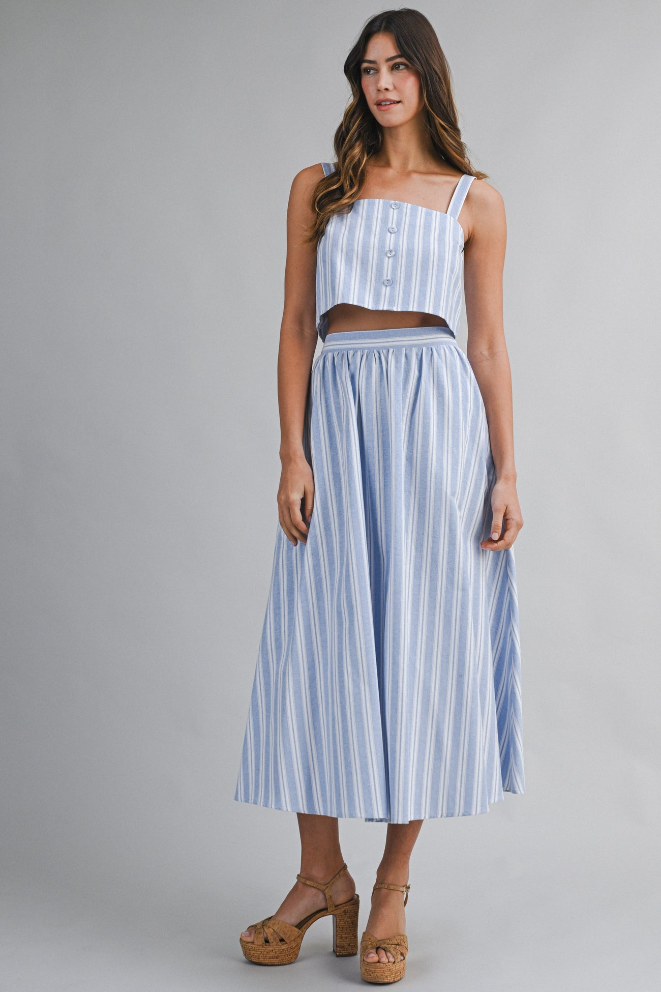 woman wearing a blue and white striped two-piece dress with a cropped top and long skirt, standing on platform heels