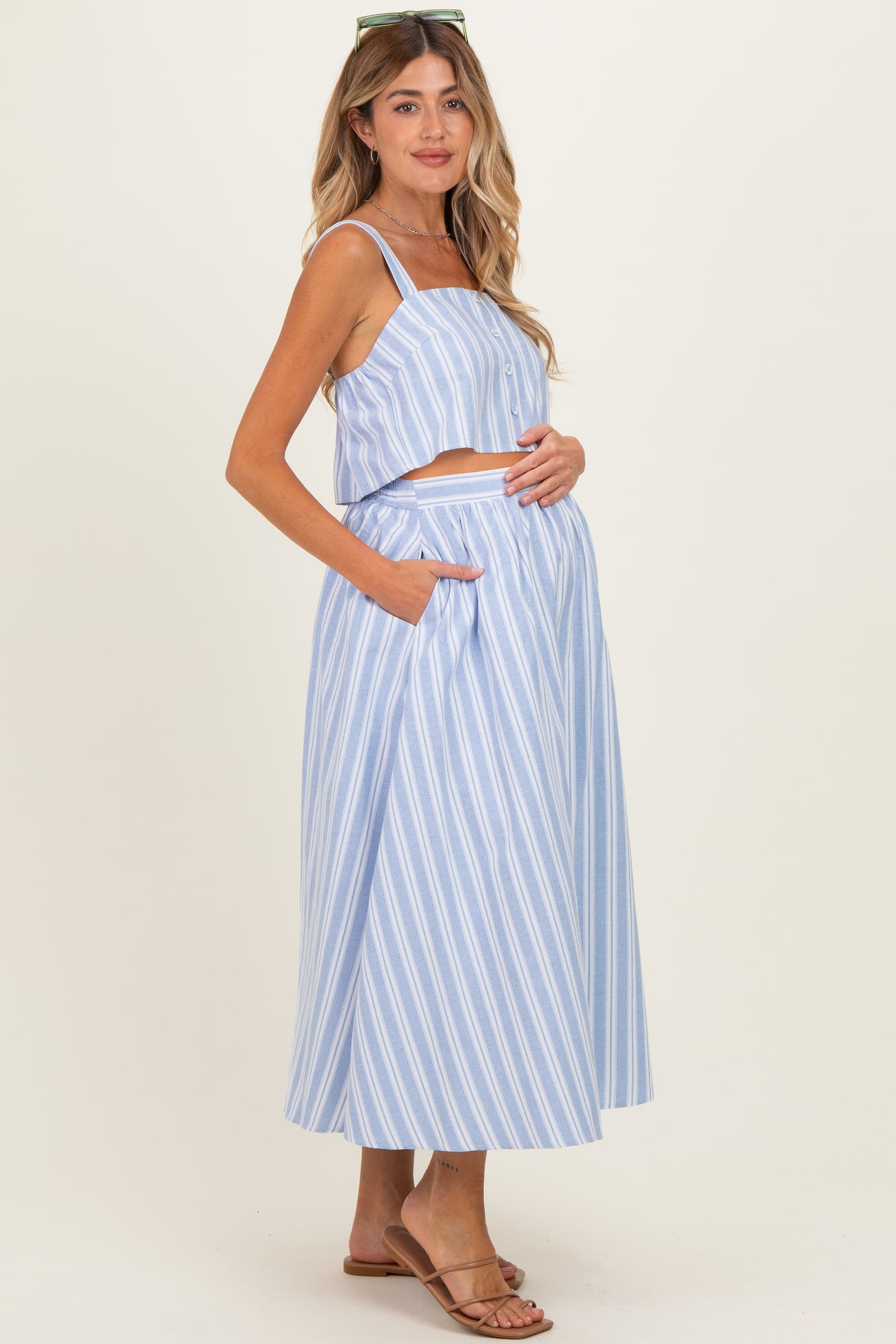 woman wearing a light blue and white striped maternity two-piece outfit with a crop top and a maxi skirt, showing her baby bump