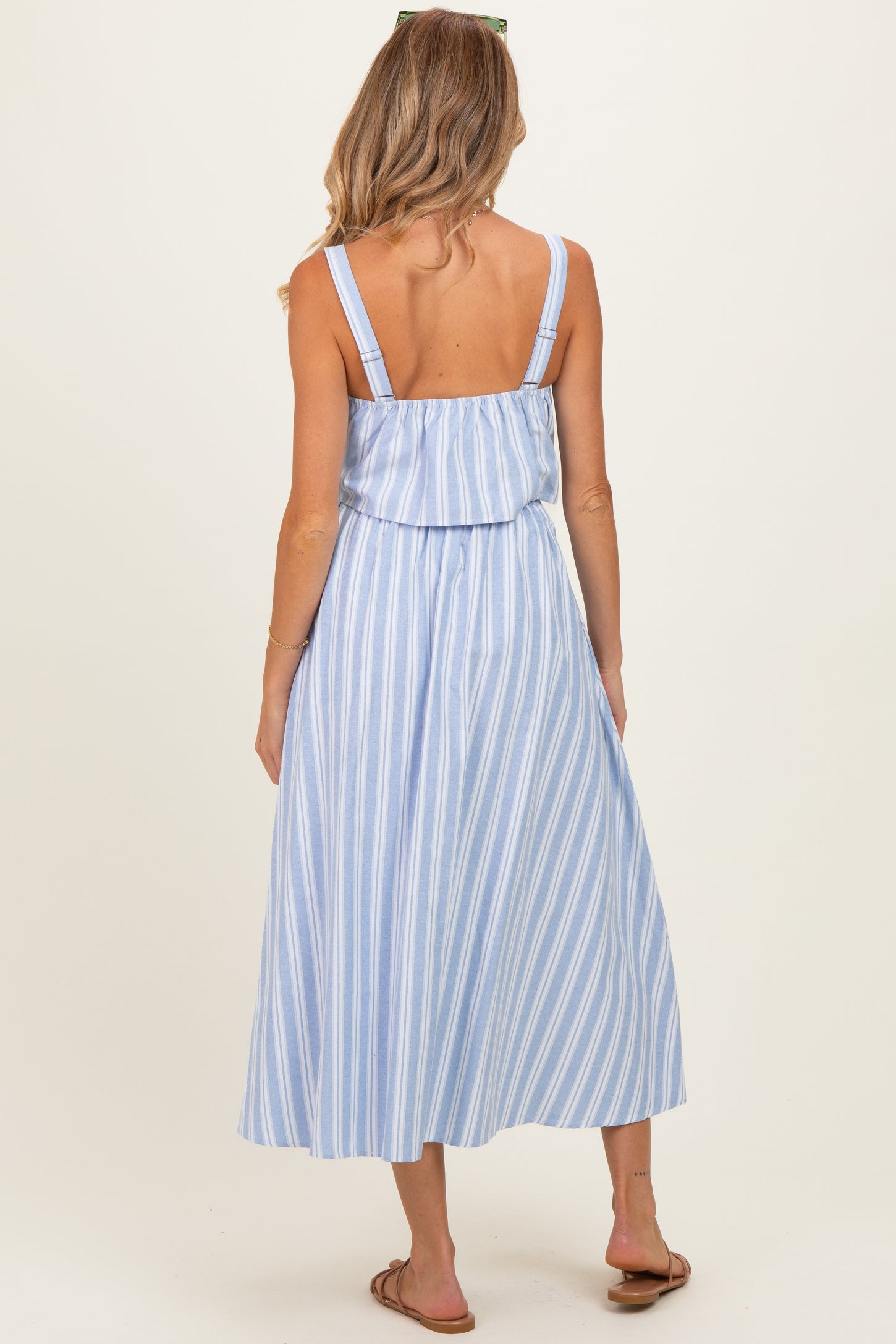 woman wearing a light blue striped maternity maxi dress, showing back view with adjustable straps and flowing skirt