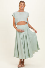 woman wearing a mint green maternity crop top and matching flowy skirt, holding her baby bump