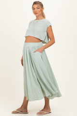 woman wearing a light green maternity crop top and a matching long pleated skirt, showing her baby bump