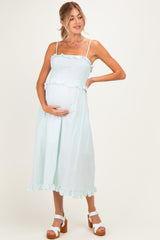woman wearing a light green maternity dress with smocked bodice and ruffled hem, holding her baby bump