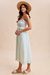 woman wearing a light green midi sundress with smocked bodice and ruffle hem, paired with a straw hat and slides