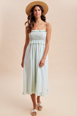 woman wearing a light green smocked midi dress with ruffle details and a straw hat
