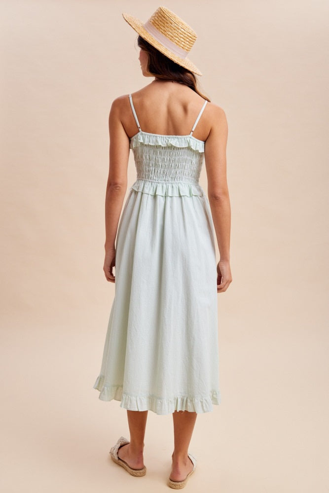 woman wearing a light green smocked back midi dress with ruffle hem and straw hat, standing with her back to the camera
