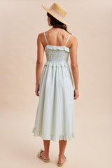 woman wearing a light green smocked back midi dress with ruffle hem and straw hat, standing with her back to the camera