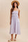 woman wearing a light purple smocked sundress with ruffled details and pockets, styled with a straw hat and sandals