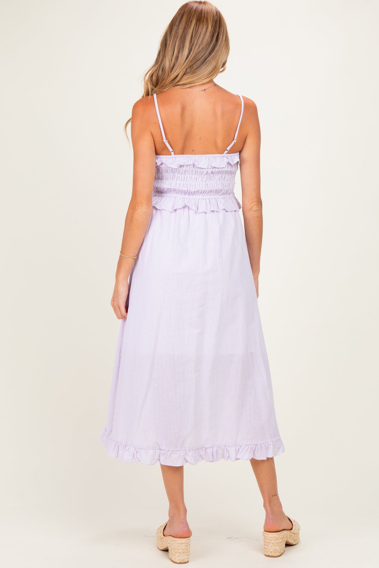 woman wearing a lavender striped maternity dress with a smocked bodice and ruffled hem, showcasing a baby bump