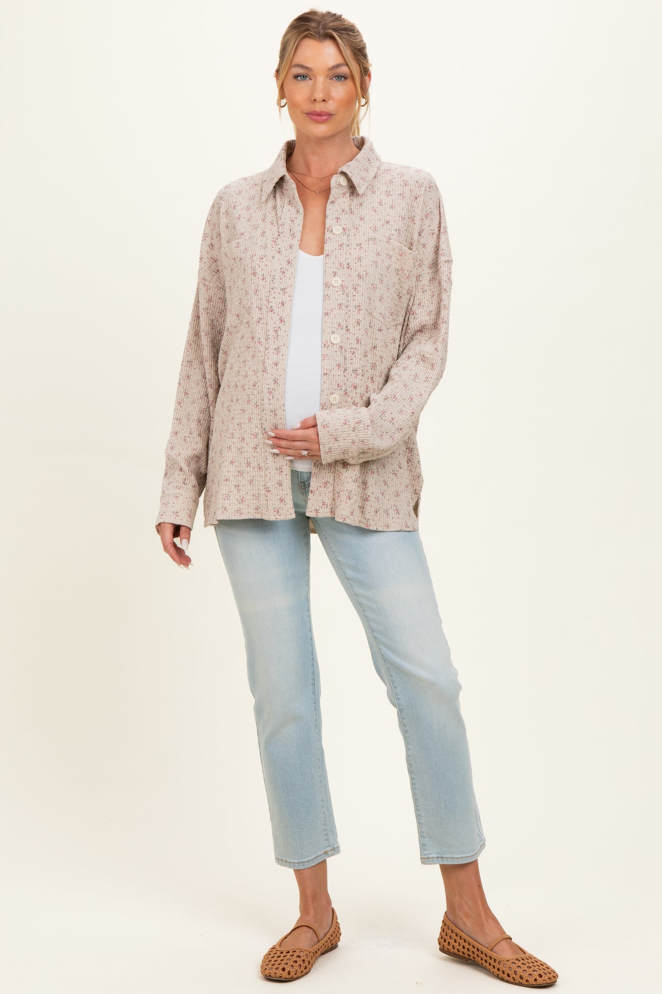 woman wearing a floral print maternity shirt with buttons and holding her baby bump, paired with light blue jeans