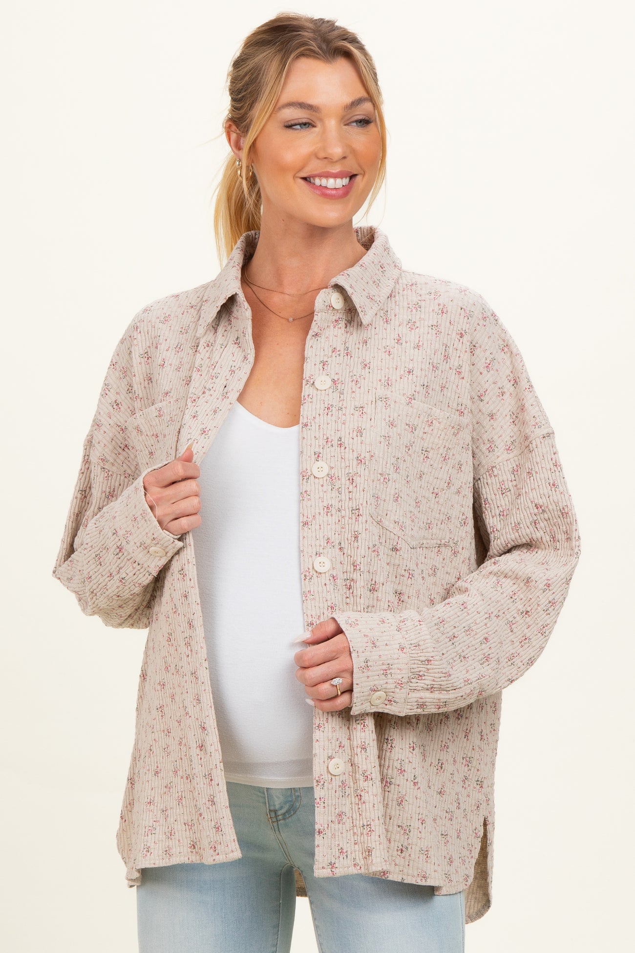 woman wearing a beige floral print maternity button-up shirt, holding it open over a white top and smiling