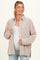 woman wearing a beige floral print maternity button-up shirt, holding it open over a white top and smiling
