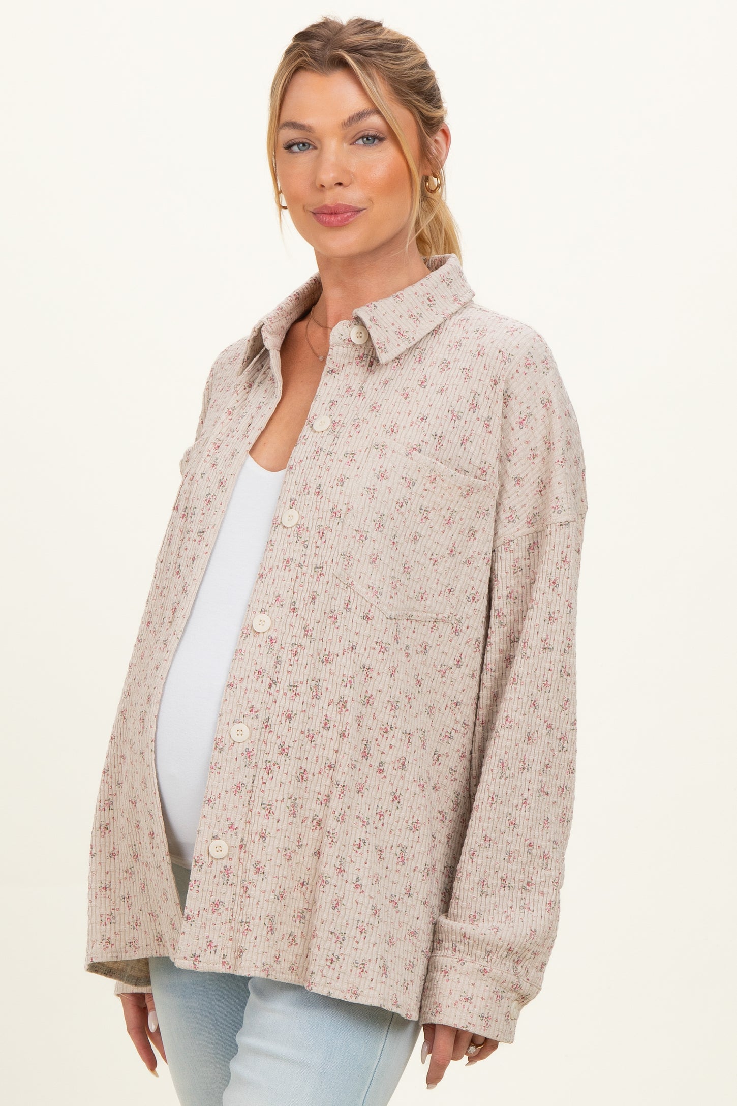 woman wearing a light pink floral maternity button-up shirt and showing her baby bump