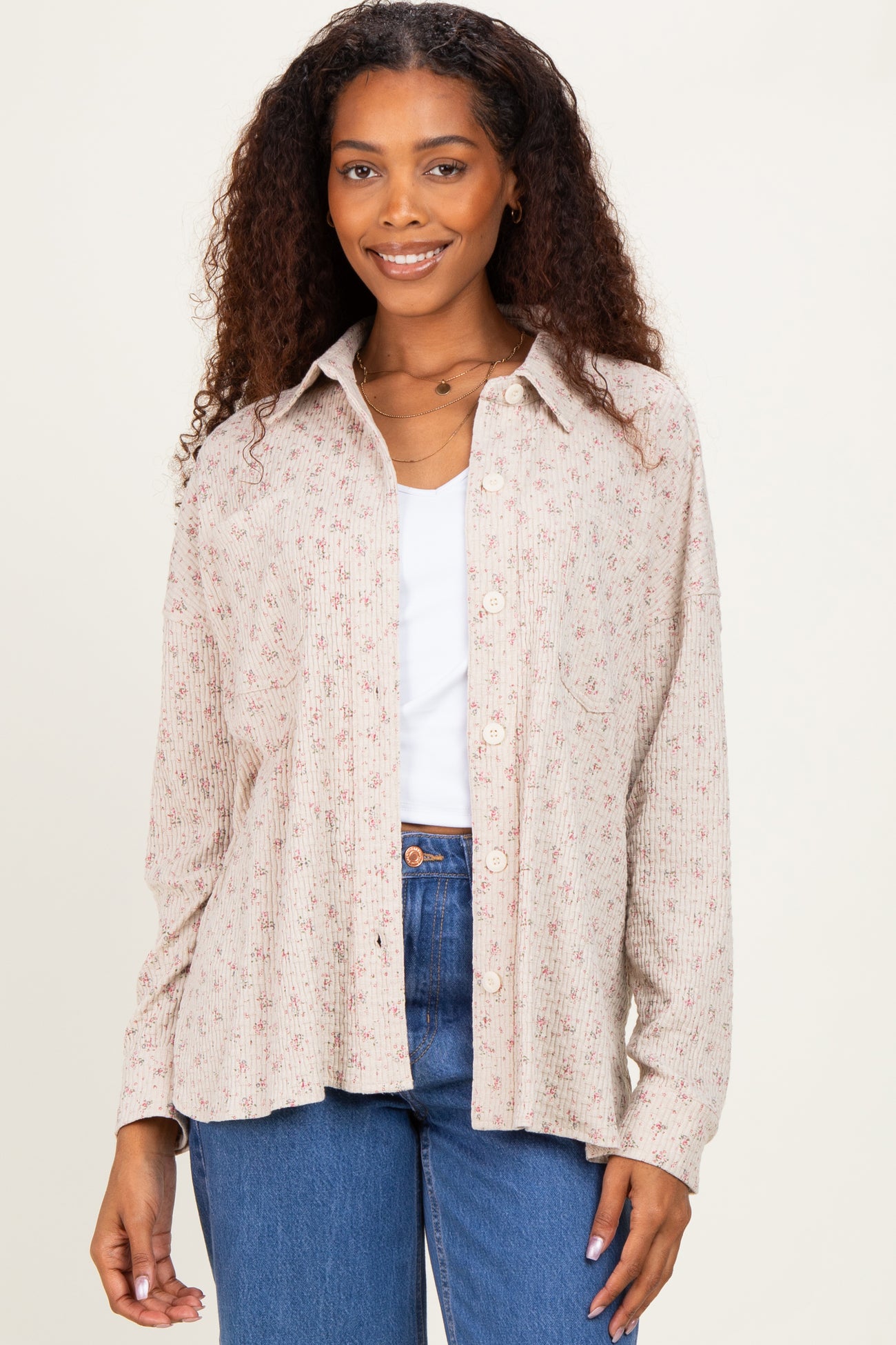 woman wearing a light beige button-up shirt with floral print and a pocket, paired with high-waisted blue jeans