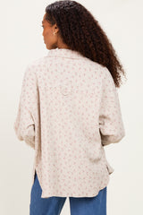 woman wearing a light beige floral patterned oversized button-up shirt, seen from the back with loose sleeves