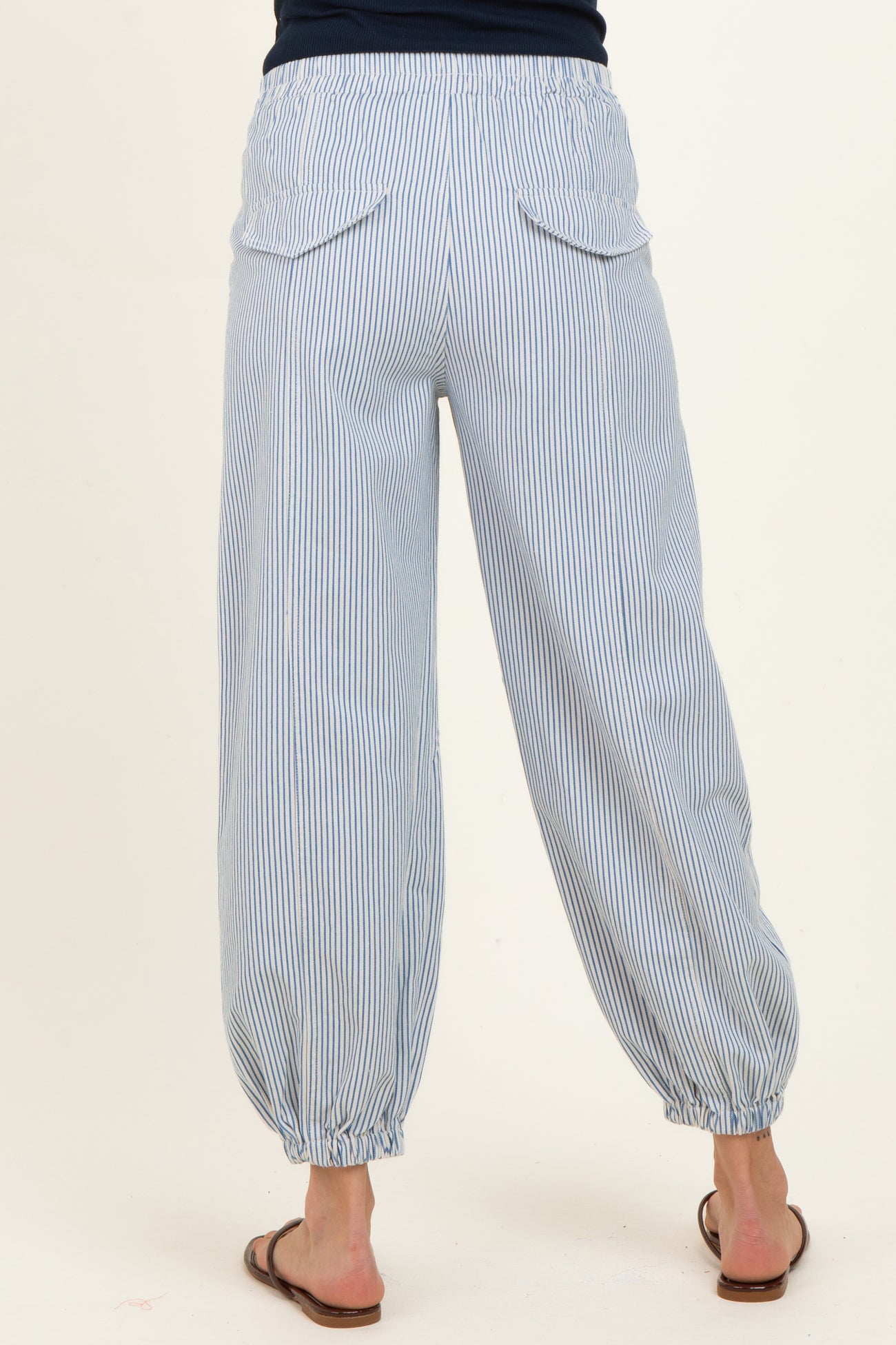 woman wearing light blue striped maternity pants with an elastic waistband and gathered cuffs, showing the back view