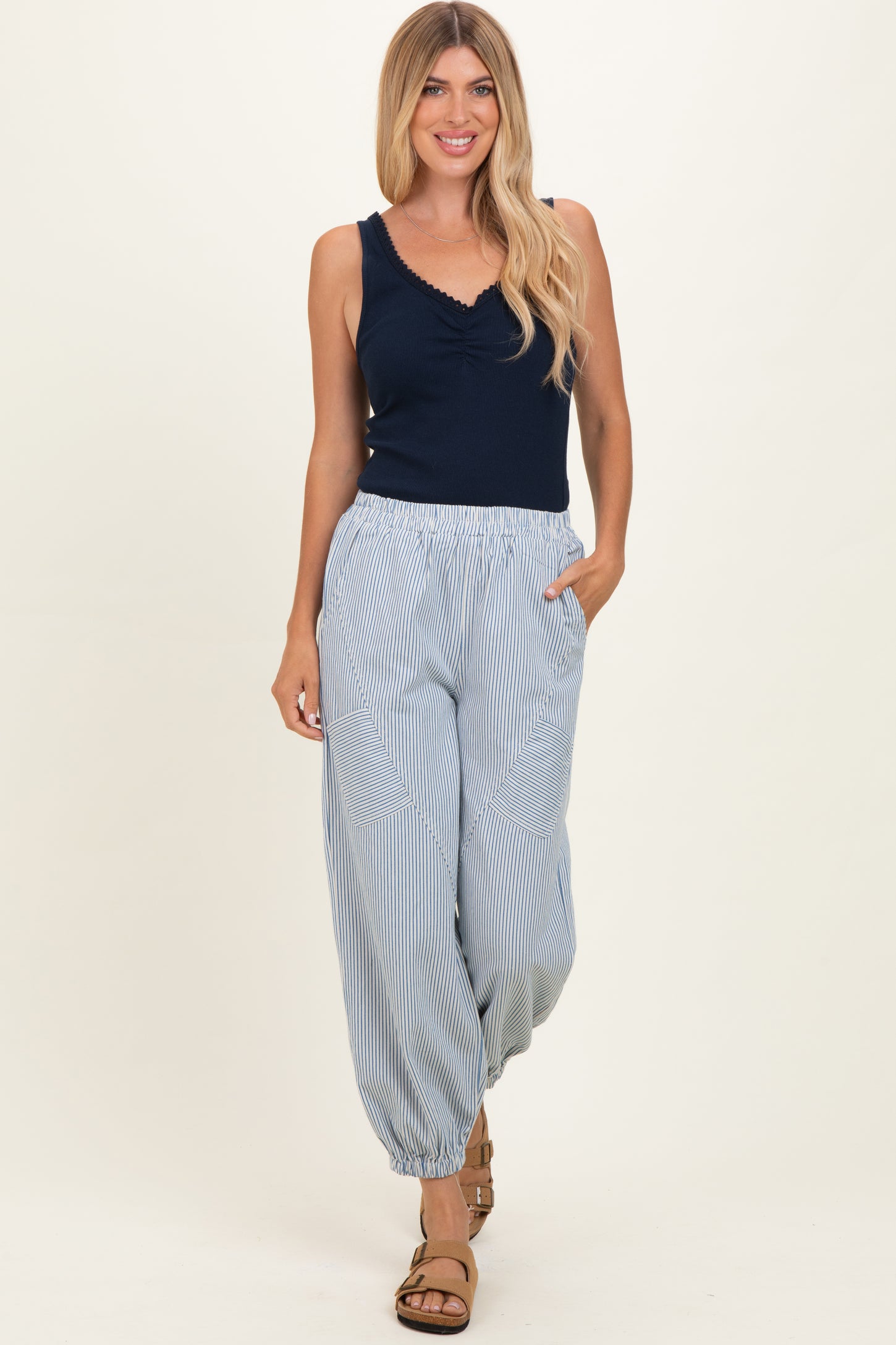 woman wearing a navy blue sleeveless top and light striped wide-leg pants with pockets