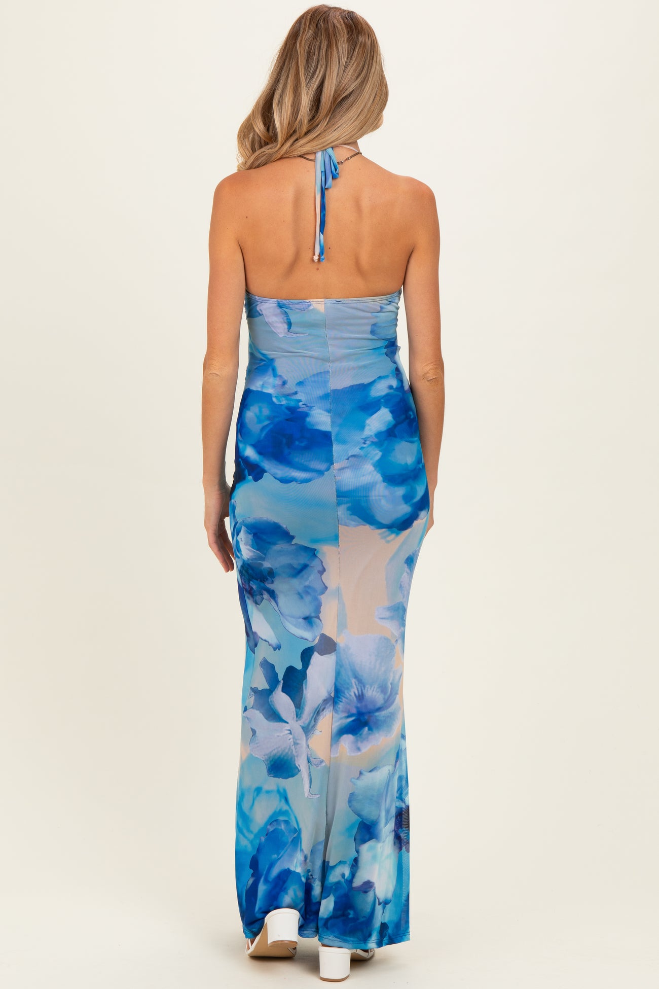 woman wearing a blue floral maternity dress with a halter neck and a long, flowing skirt, showcasing a baby bump