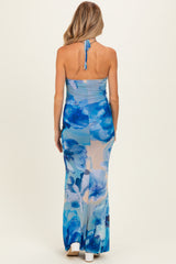 woman wearing a blue floral maternity dress with a halter neck and a long, flowing skirt, showcasing a baby bump