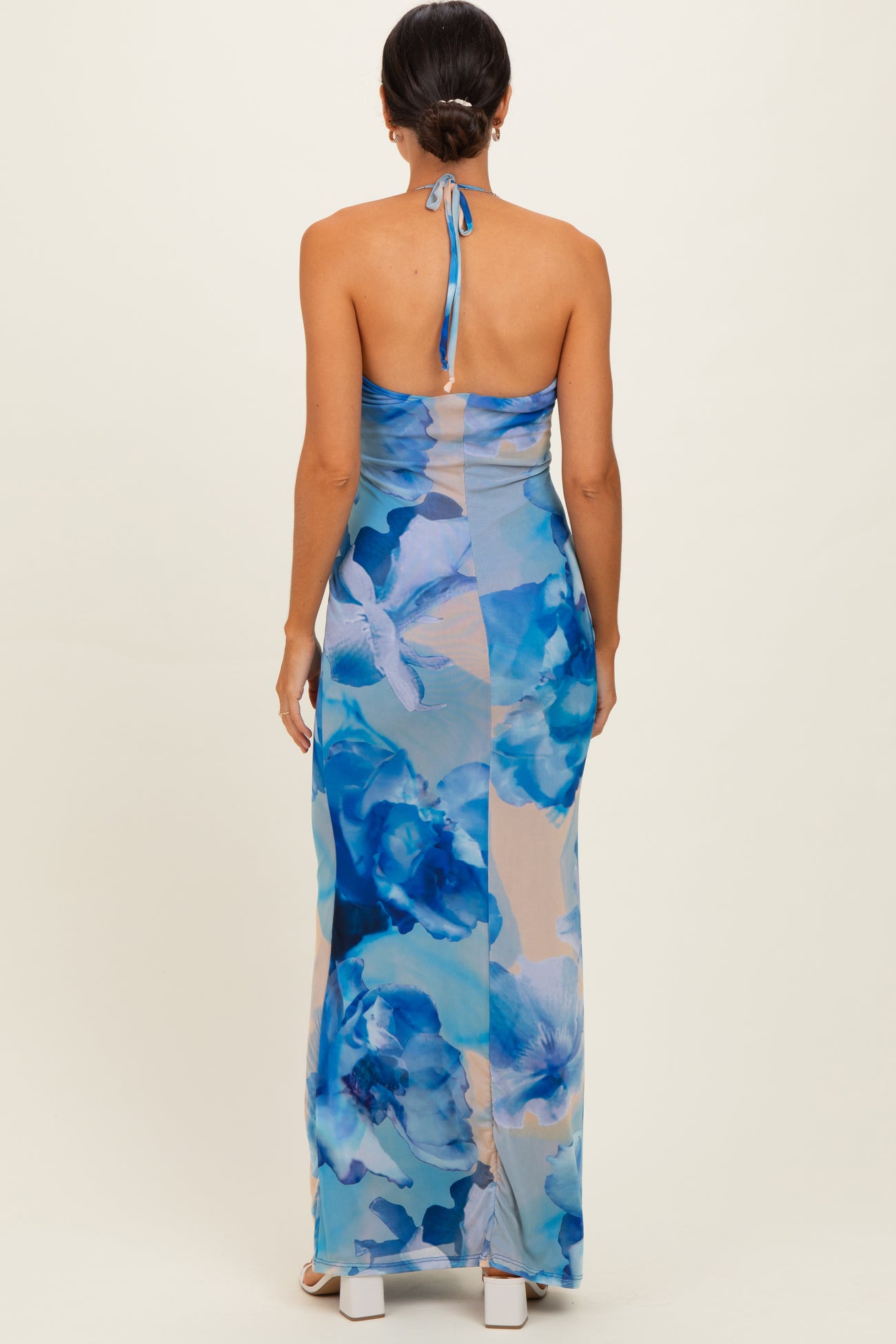 woman wearing a backless blue floral maxi dress with a halter neck and a fitted silhouette