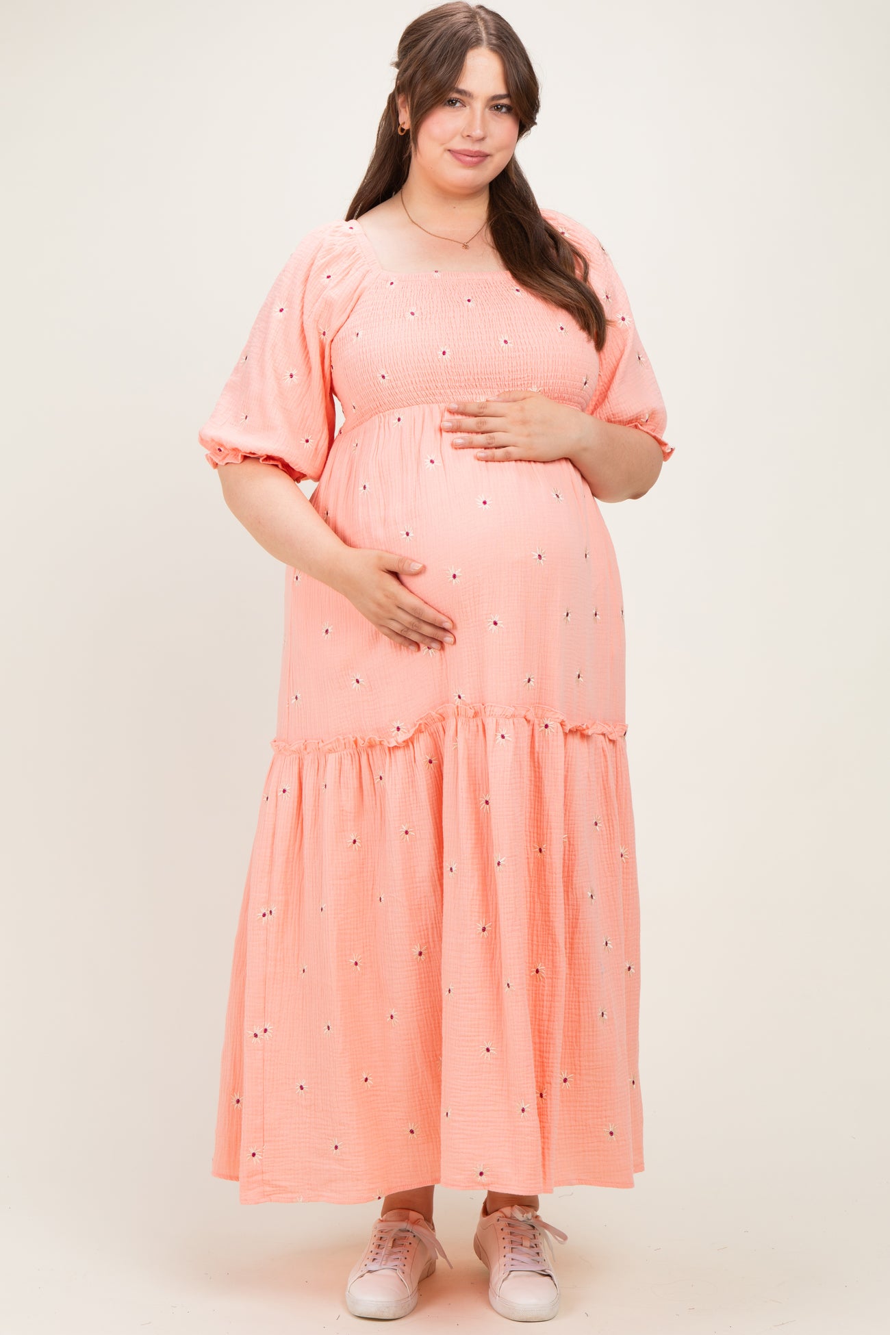 woman wearing a coral maternity dress with short puff sleeves and tiered skirt, holding her baby bump
