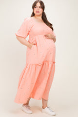 woman wearing a coral maternity plus maxi dress with puff sleeves and floral embroidery, holding her baby bump