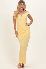 woman wearing a pale yellow off-shoulder ruched maxi dress with a decorative neckline and a fitted silhouette