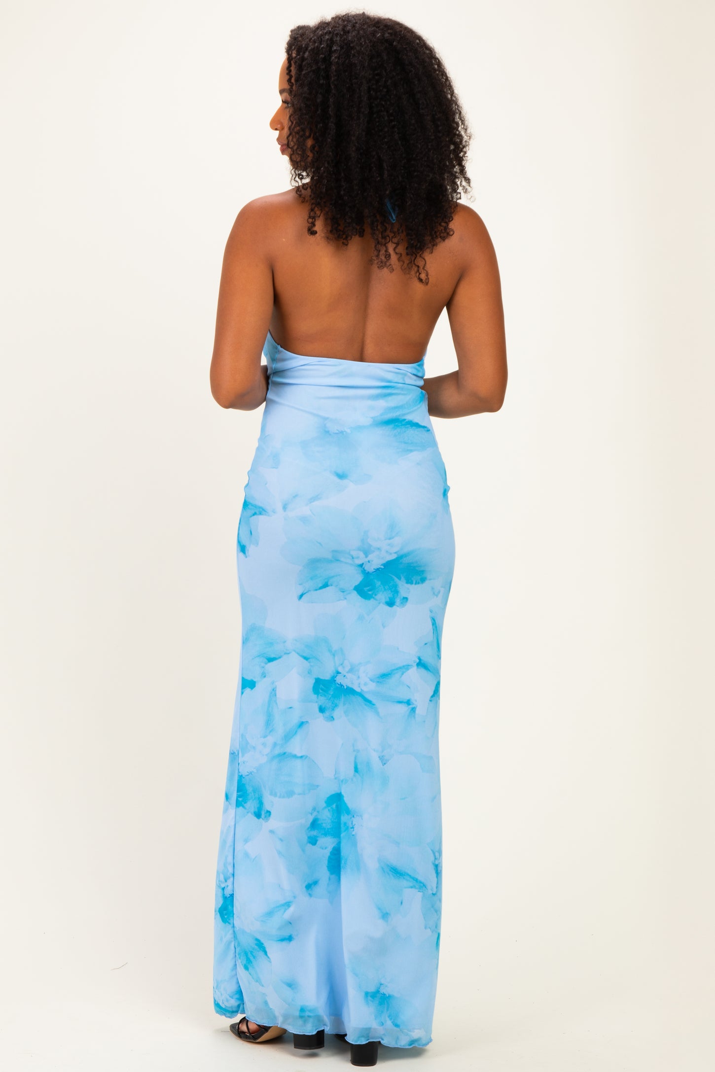 woman wearing a backless blue floral maxi dress with a fitted silhouette and flowing skirt