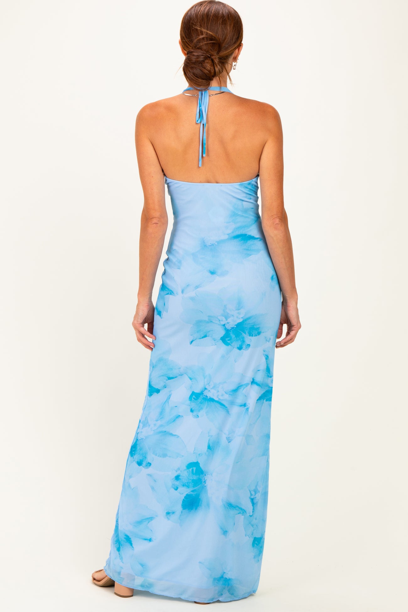 woman wearing a light blue floral maxi dress with a halter neck and open back, showing a smooth fit and flowy silhouette