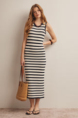 woman wearing a black and white striped ribbed maxi dress, holding a woven tote bag and standing with one hand on her hip
