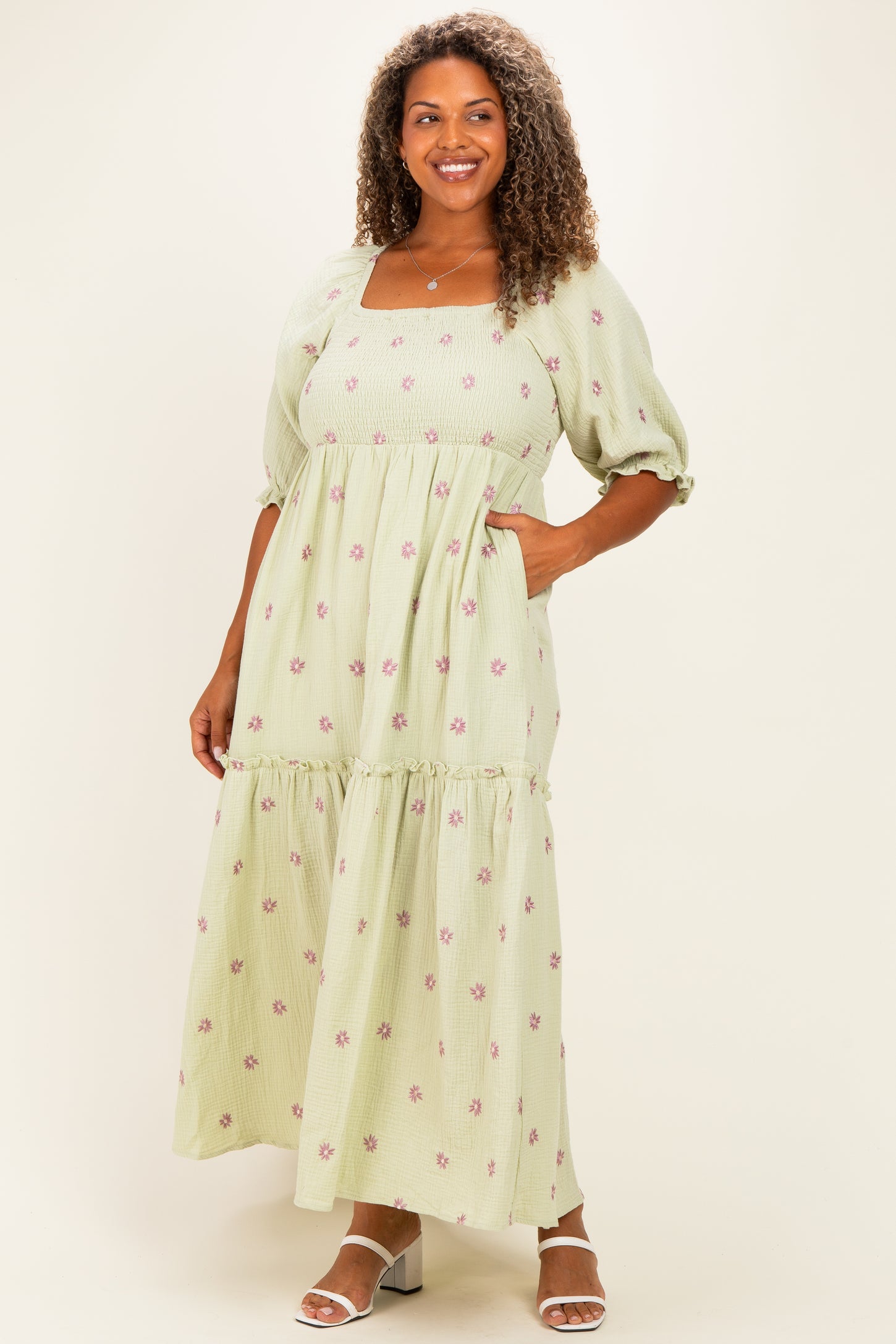 woman wearing a light green plus size maxi dress with floral embroidery and puff sleeves, standing with hands in pockets