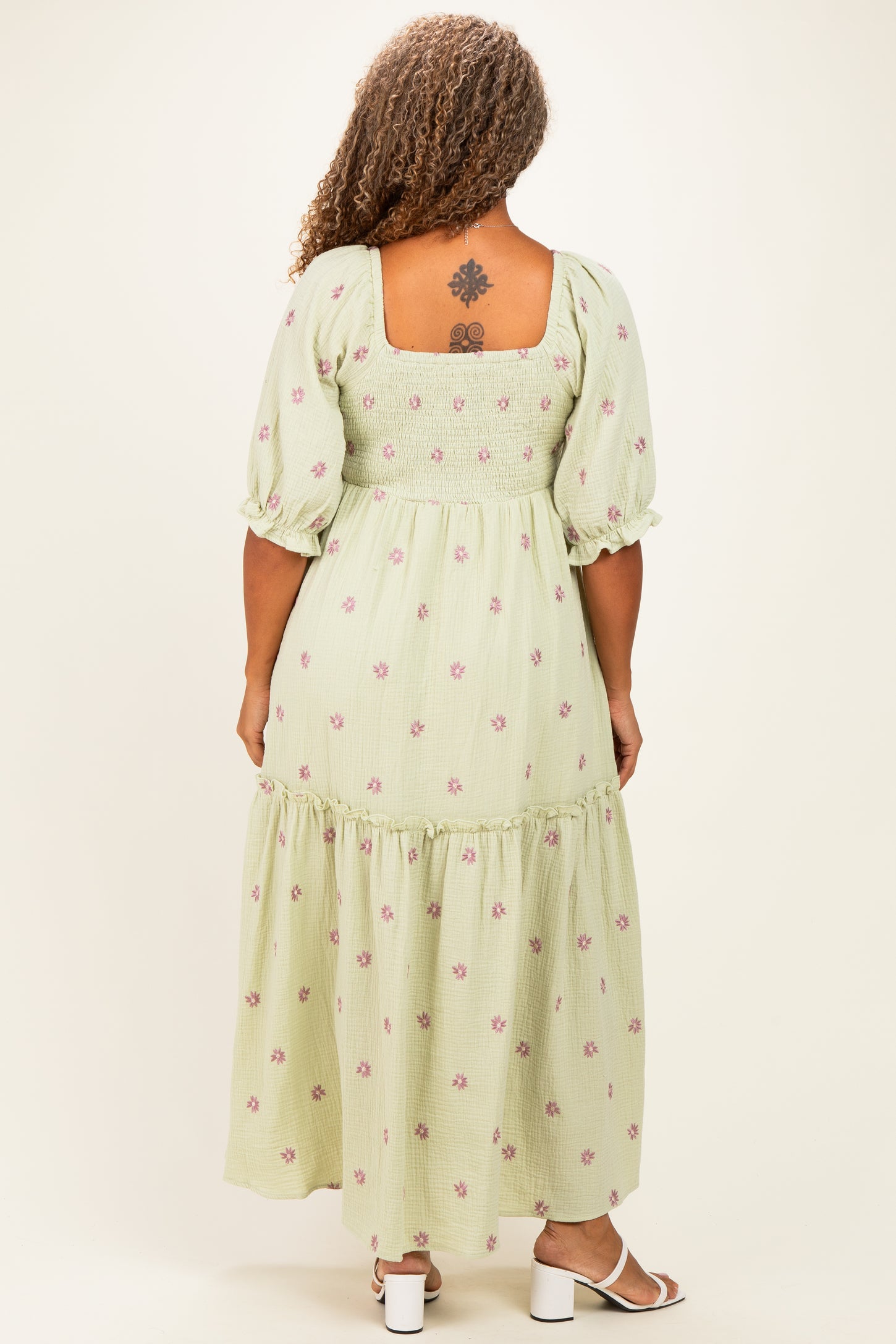 woman wearing a green floral printed plus size maxi dress with puff sleeves and a square back, showing a tattoo on her back