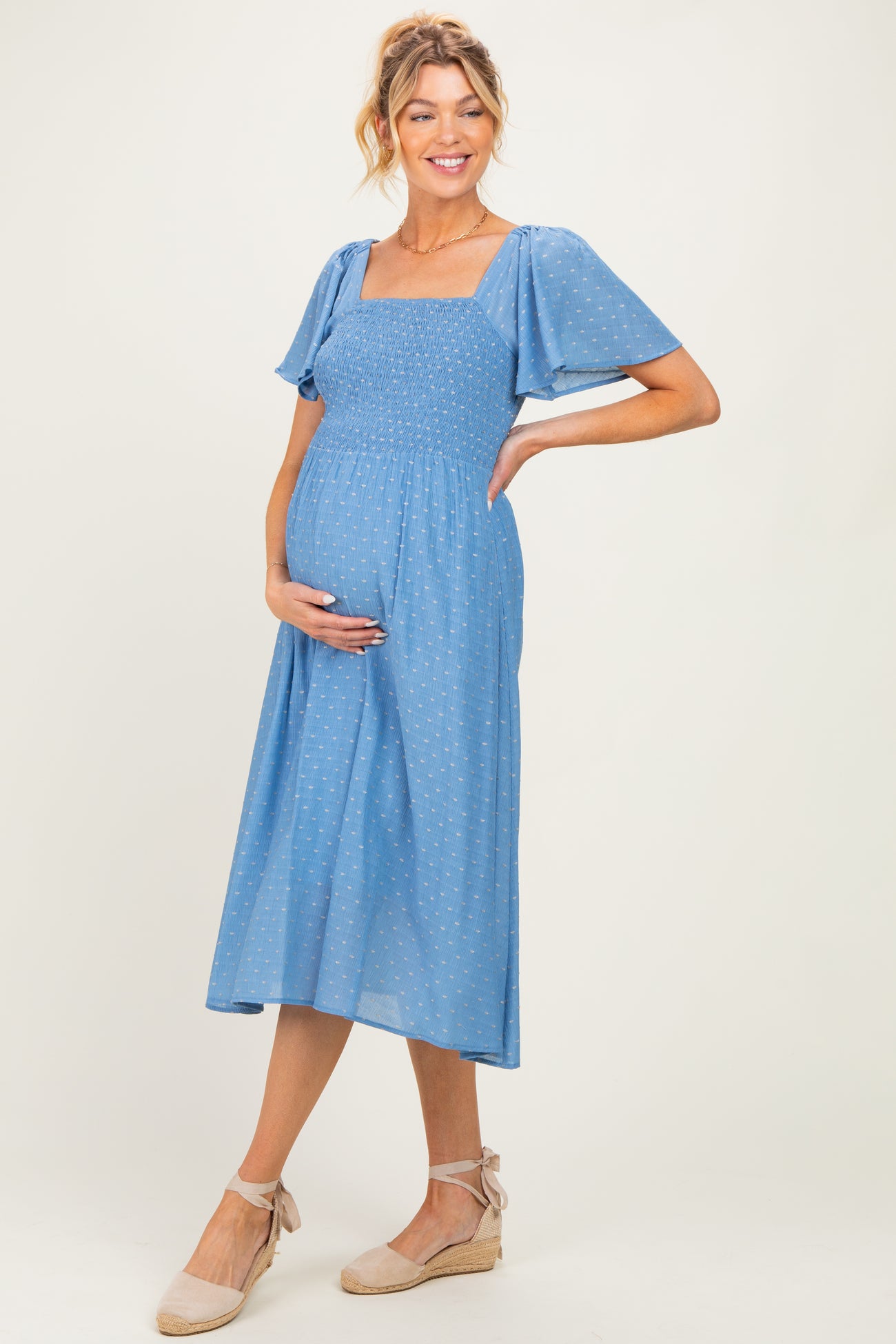 woman wearing a light blue maternity dress with short flutter sleeves and a smocked bodice, showing her baby bump