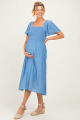 woman wearing a light blue maternity dress with short flutter sleeves and a smocked bodice, showing her baby bump