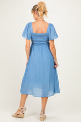 woman wearing a blue dot print maternity dress with short puff sleeves and a smocked waist, showing a baby bump
