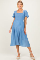 woman wearing a light blue maternity dress with short flutter sleeves and a square neckline, featuring polka dot details and a baby bump