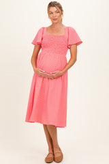 woman wearing a pink smocked maternity dress with flutter sleeves and a visible baby bump