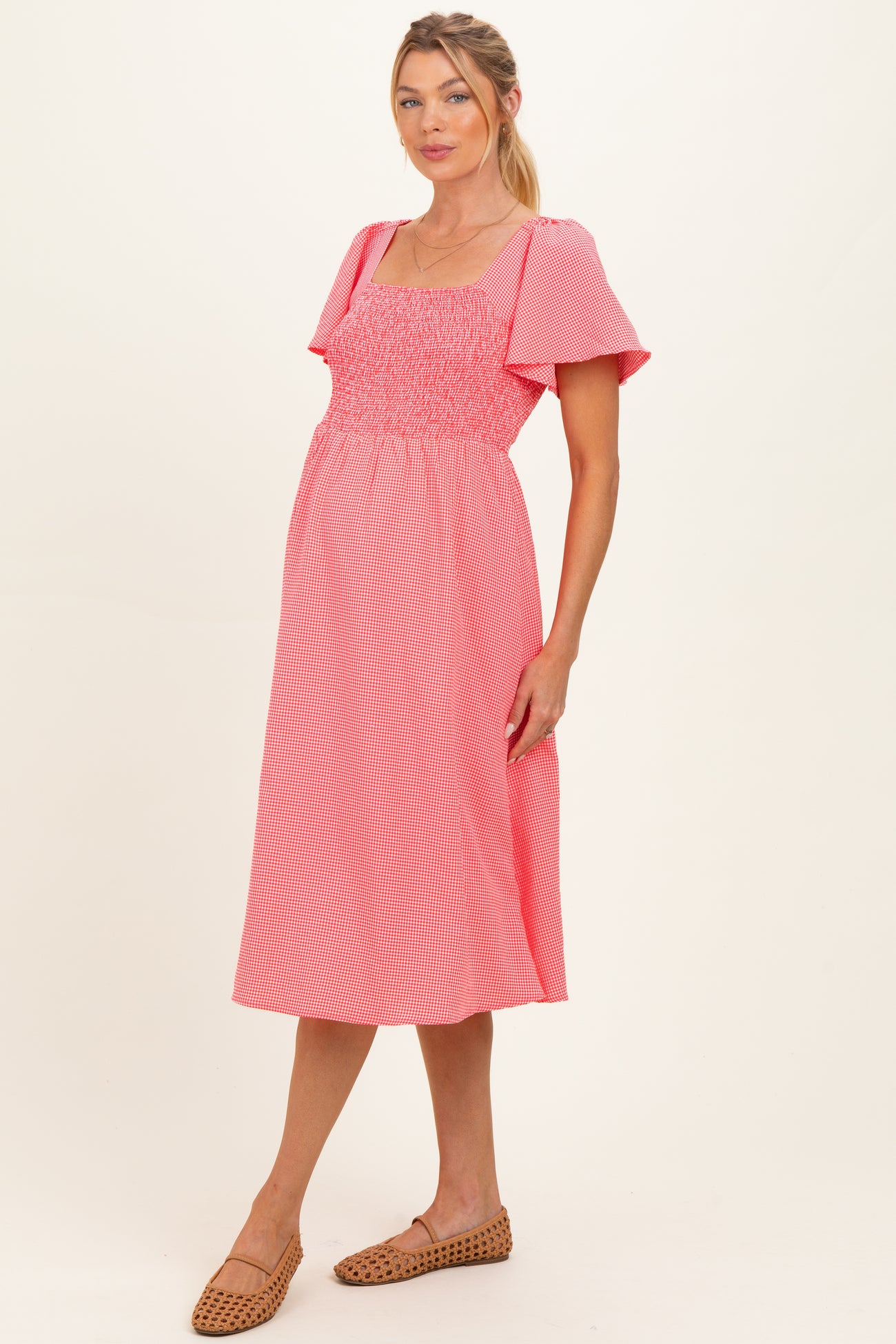 woman wearing a coral and white striped maternity dress with puff sleeves and a smocked bodice, showing her baby bump
