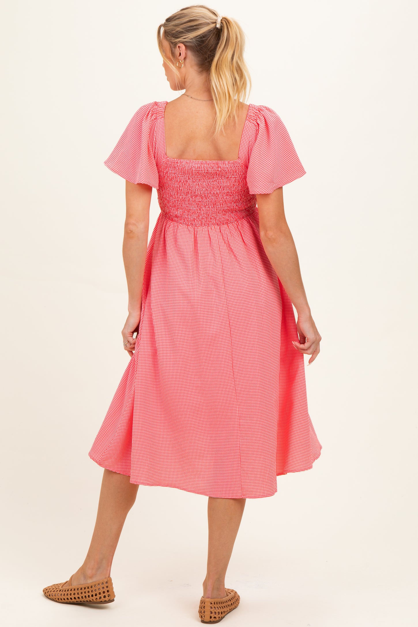 woman wearing a coral and white striped maternity dress with short puff sleeves and a smocked bodice, showing a baby bump
