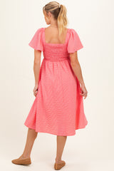 woman wearing a coral and white striped maternity dress with short puff sleeves and a smocked bodice, showing a baby bump