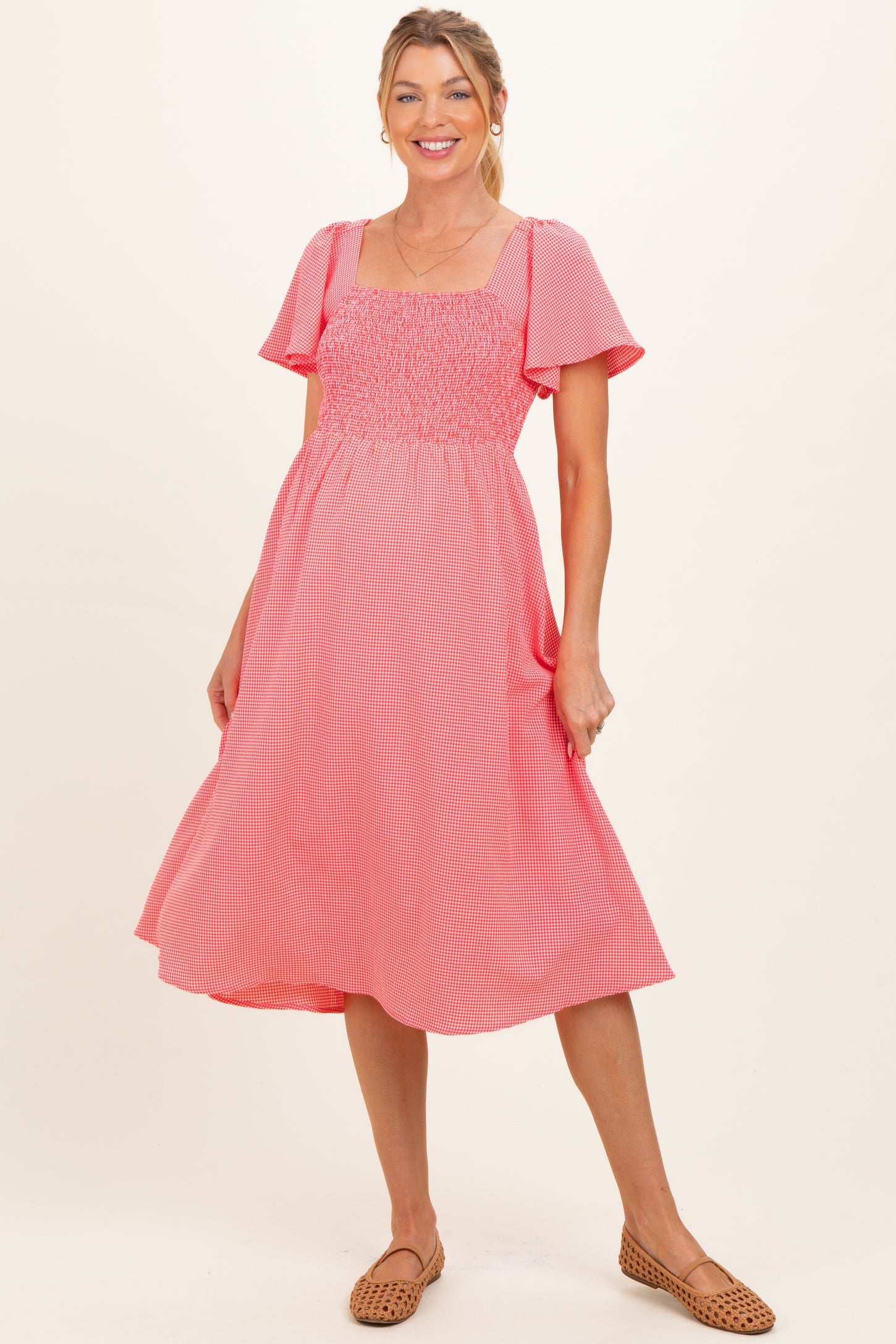 woman wearing a pink striped maternity dress with short flutter sleeves and a smocked bodice, showing her baby bump