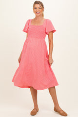 woman wearing a pink striped maternity dress with short flutter sleeves and a smocked bodice, showing her baby bump