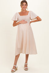 woman wearing a light pink maternity dress with short puff sleeves and a square neckline, holding her baby bump