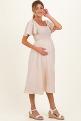woman wearing a blush pink maternity dress with flutter sleeves and a smocked bodice, holding her baby bump