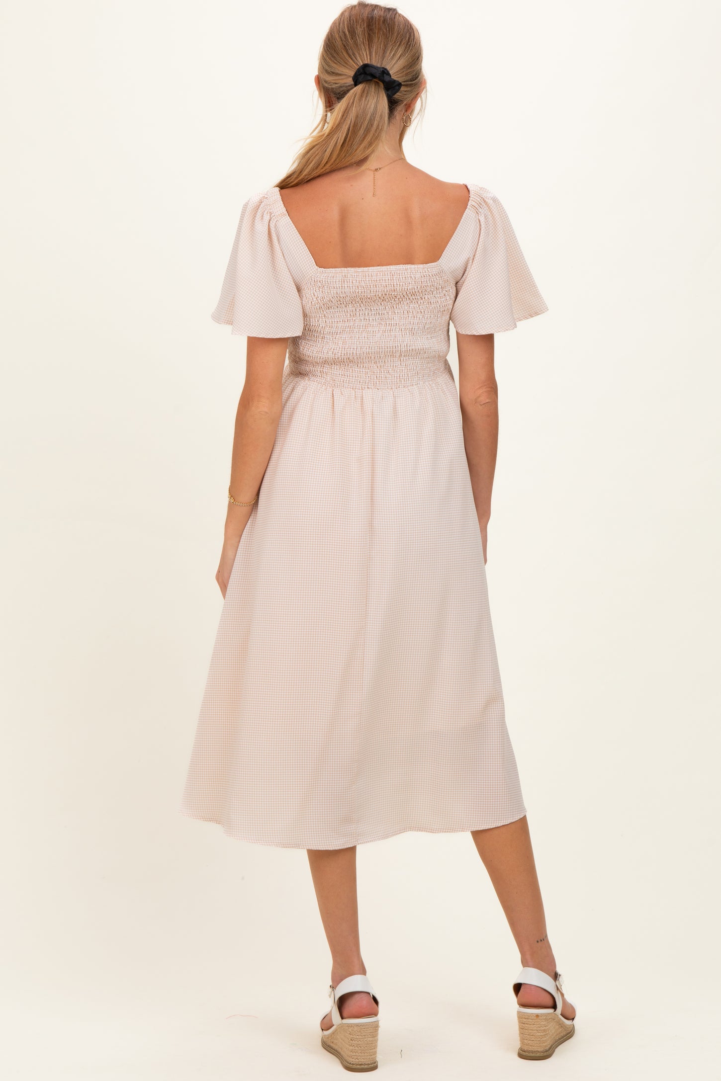 woman wearing a light pink maternity dress with short puff sleeves and a smocked bodice, showing a baby bump from behind