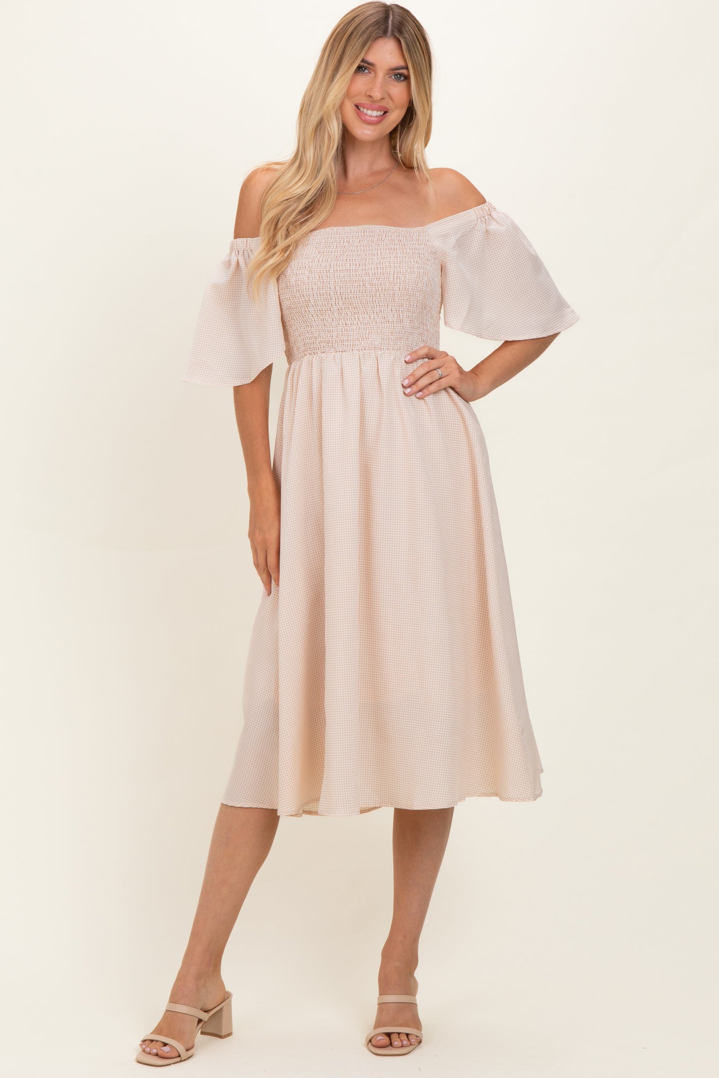 woman wearing a light beige off-the-shoulder midi dress with a smocked bodice and flowy sleeves.