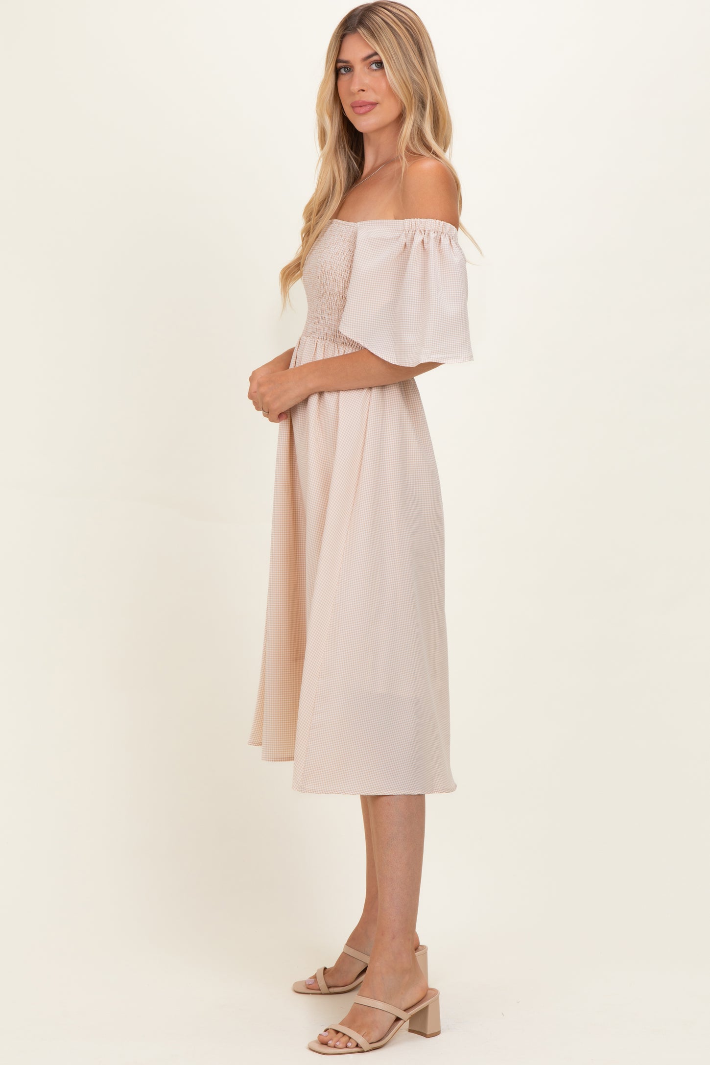 woman wearing a blush off-the-shoulder midi dress with puff sleeves and a smocked bodice