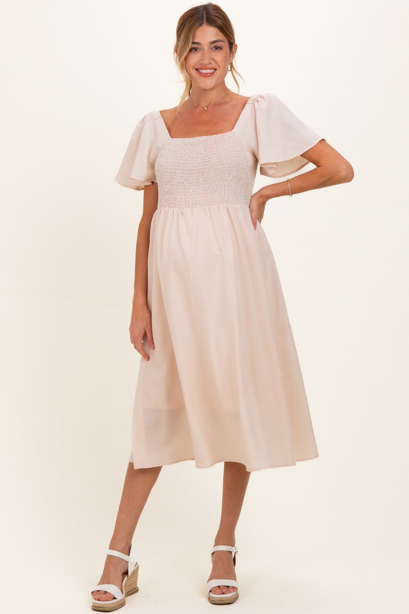 woman wearing a light pink maternity dress with a smocked bodice and puff sleeves, showing a baby bump