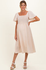 woman wearing a light pink maternity dress with a smocked bodice and puff sleeves, showing a baby bump
